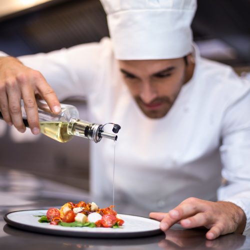 Handsome chef pouring olive oil on meal in a commercial kitchen